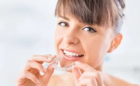 Invisalign patient holding her retainers with two hands and smiling.