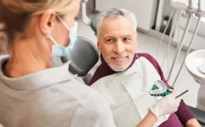 Dental patient sitting in the dentists chair with a the dentist showing a mold.