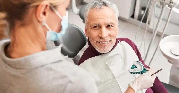 Dental patient sitting in the dentists chair with a the dentist showing a mold.
