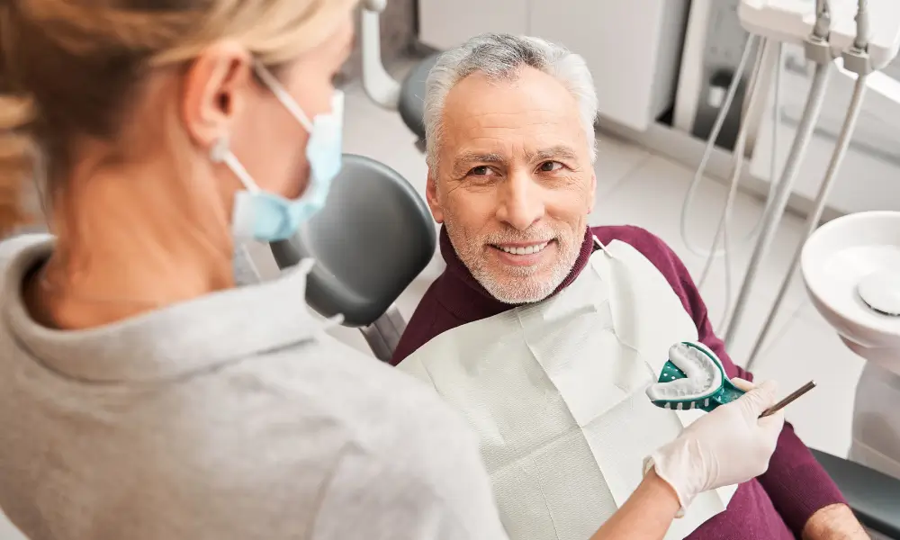 Dental patient sitting in the dentists chair with a the dentist showing a mold.
