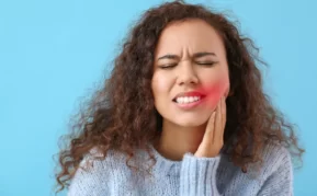 Young woman with her hand on her left cheek clearly in pain from her teeth.