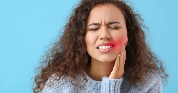 Young woman with her hand on her left cheek clearly in pain from her teeth.